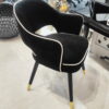 Tapicerowane czarne krzesło obite welurem z białym wykończeniem i złotymi nogami