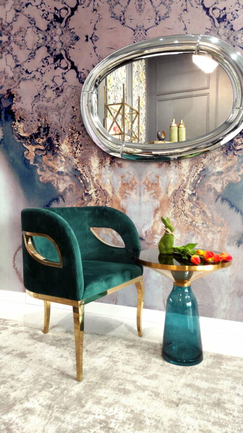 Piękny welurowy fotel na trzech złotych nogac, a nad nim duże wiszące lustro dekoracdyjne